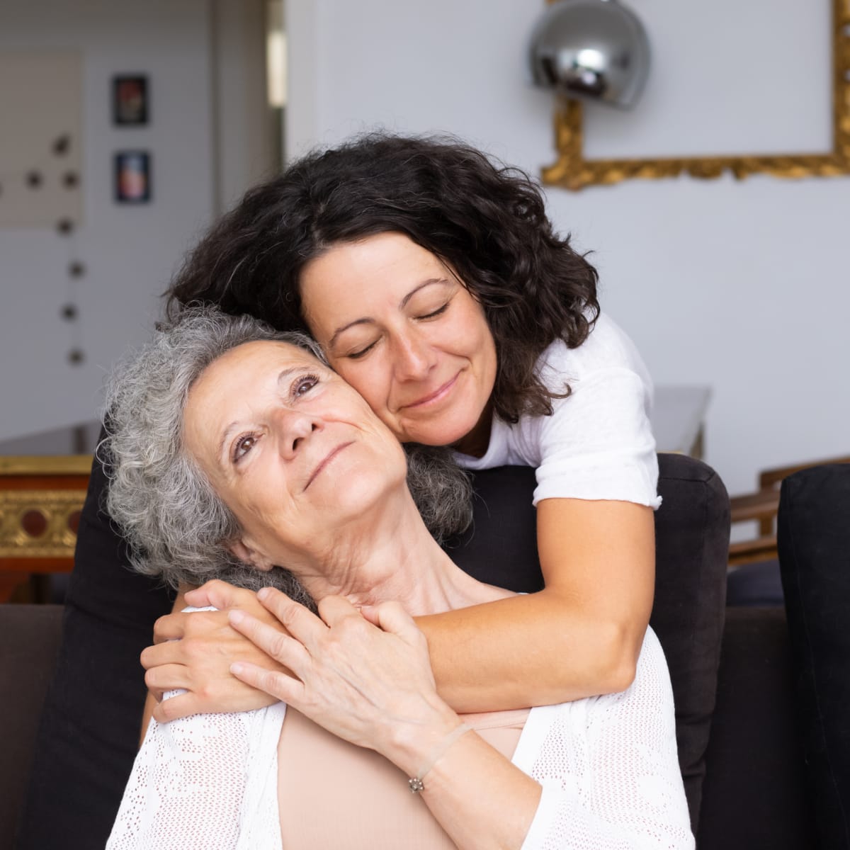 Older woman being embraced by a younger woman from behind.