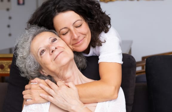 Older woman being embraced by a younger woman from behind.